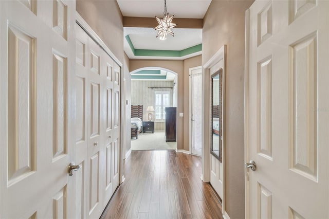 foyer with baseboards, a tray ceiling, arched walkways, dark wood-type flooring, and a chandelier