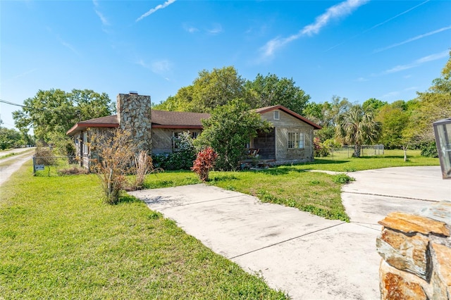 view of front of property featuring a front lawn, concrete driveway, fence, and a chimney