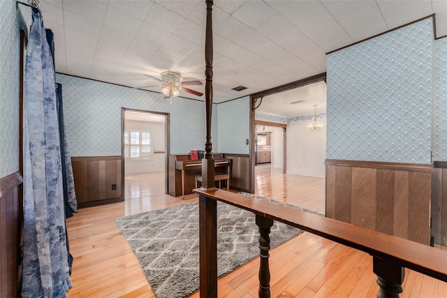 interior space featuring visible vents, a ceiling fan, hardwood / wood-style flooring, wainscoting, and wallpapered walls