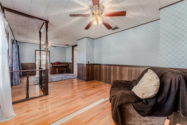sitting room with visible vents, wallpapered walls, hardwood / wood-style floors, wainscoting, and a ceiling fan
