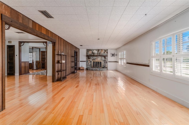 unfurnished living room featuring visible vents, wooden walls, baseboards, a stone fireplace, and light wood-style flooring