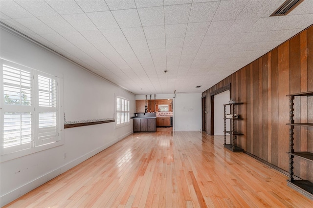 unfurnished living room with visible vents, wood walls, light wood-type flooring, and baseboards