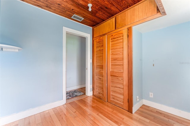 unfurnished bedroom with light wood-type flooring, visible vents, a closet, wooden ceiling, and baseboards