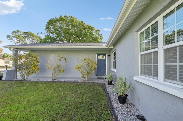 view of exterior entry with a lawn and stucco siding