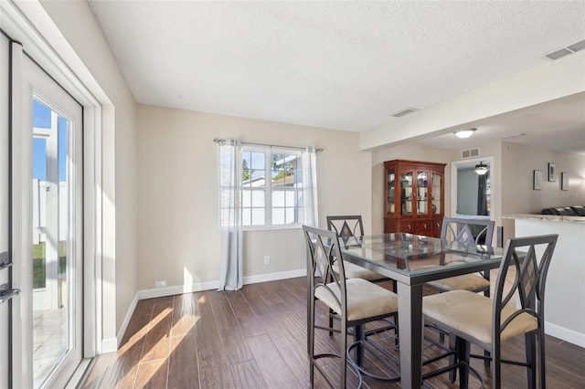 dining area with baseboards, dark wood-style floors, visible vents, and a textured ceiling