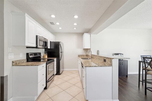 kitchen with light stone counters, a peninsula, stainless steel appliances, white cabinetry, and a sink