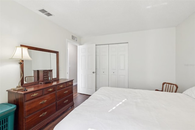 bedroom with dark wood-type flooring, visible vents, and a closet