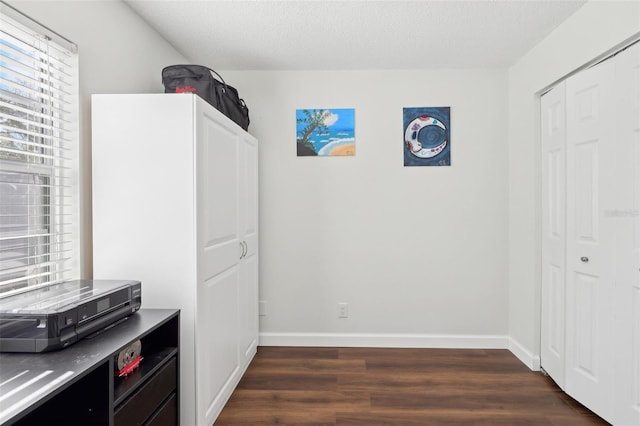 interior space featuring a closet, baseboards, a textured ceiling, and dark wood finished floors