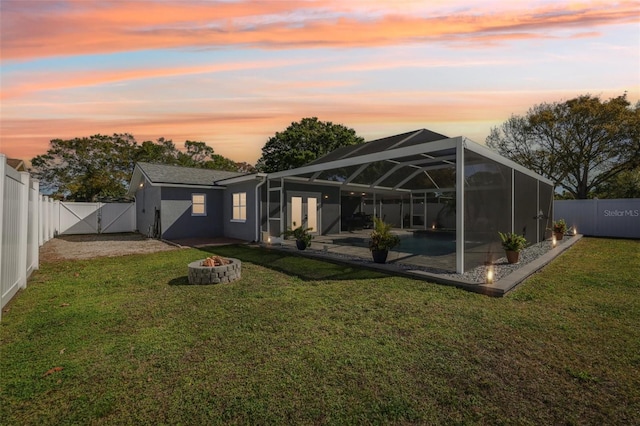 back of house at dusk featuring a gate, a fenced backyard, a fire pit, a lanai, and a patio area