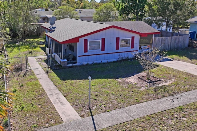 view of front facade featuring a front lawn, a sunroom, fence, and roof with shingles