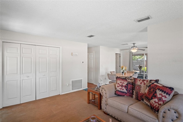 carpeted living room with a ceiling fan, visible vents, and a textured ceiling