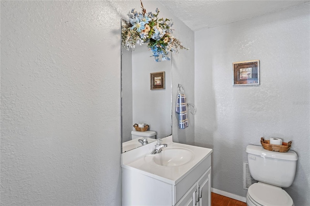 half bath with toilet, vanity, and a textured wall