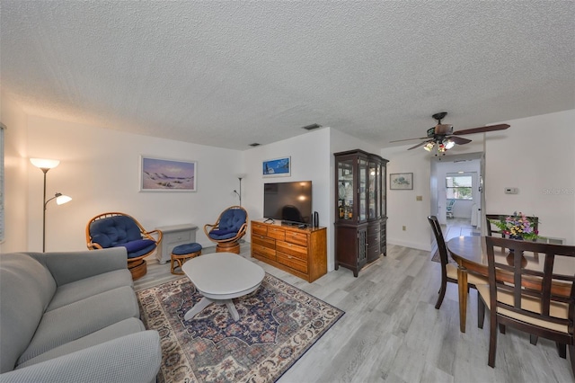 living room with visible vents, a textured ceiling, a ceiling fan, and light wood finished floors