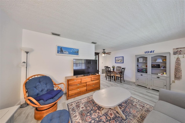 living room with visible vents, light wood-style flooring, a textured ceiling, and a ceiling fan