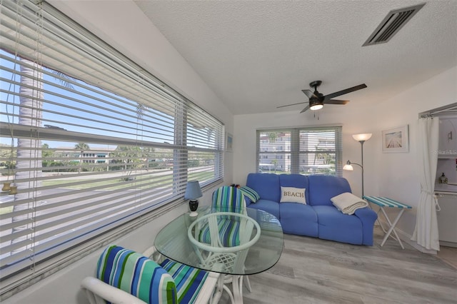 living room with ceiling fan, visible vents, a textured ceiling, and wood finished floors