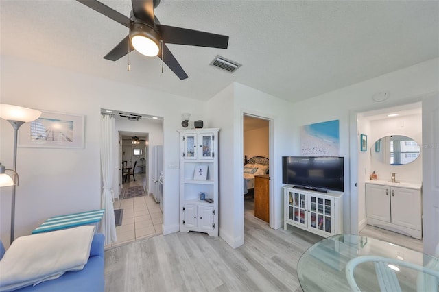 living area with baseboards, visible vents, light wood-style flooring, ceiling fan, and a textured ceiling