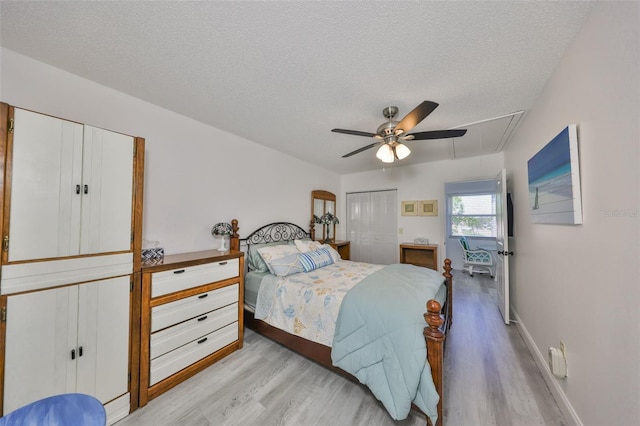 bedroom with baseboards, ceiling fan, attic access, light wood-style floors, and a textured ceiling