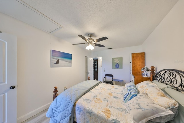 bedroom with visible vents, baseboards, attic access, wood finished floors, and a textured ceiling