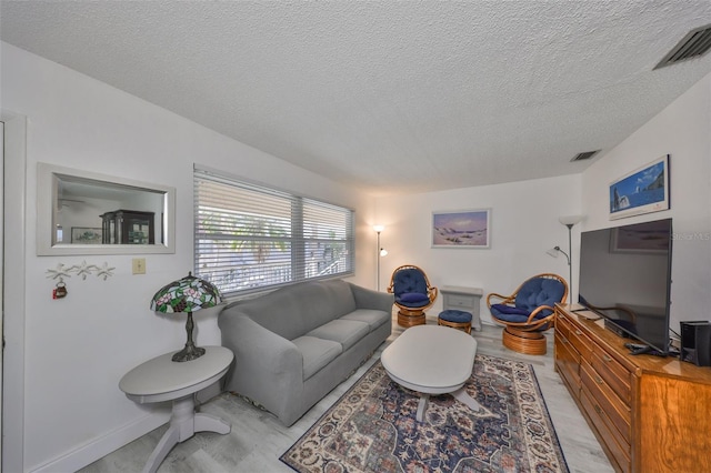 living room with light wood-type flooring, visible vents, and a textured ceiling