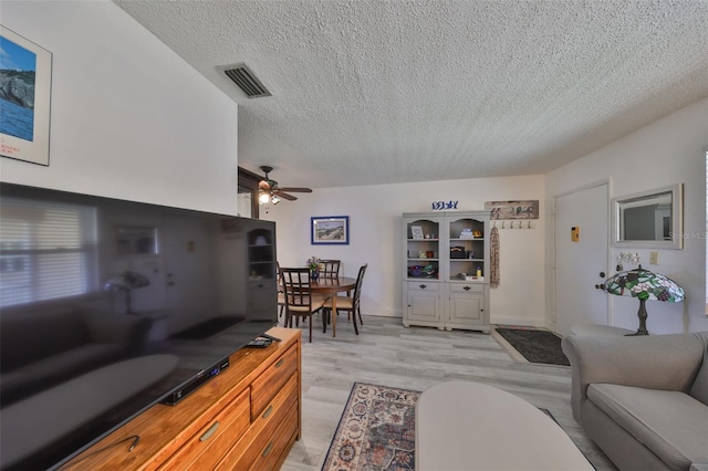 living room featuring visible vents, a textured ceiling, light wood-style flooring, and a ceiling fan