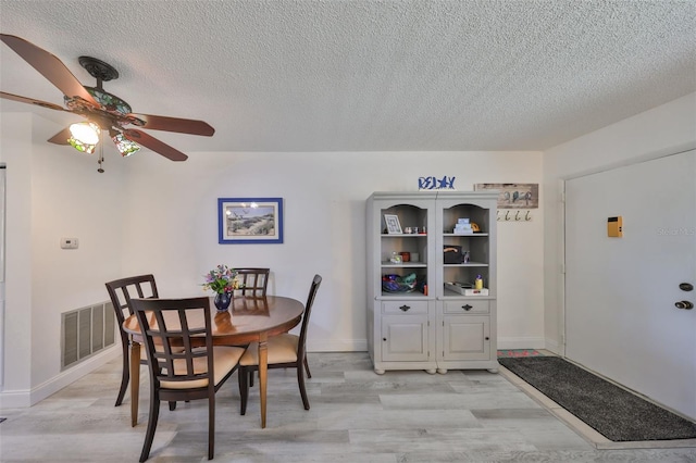 dining space featuring a textured ceiling, light wood-style flooring, visible vents, and ceiling fan