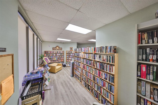 sitting room featuring bookshelves, wood finished floors, and a drop ceiling