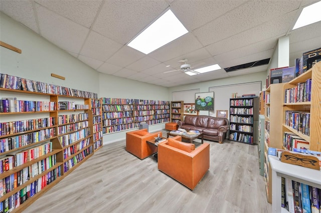 home office with wood finished floors, wall of books, a drop ceiling, and ceiling fan