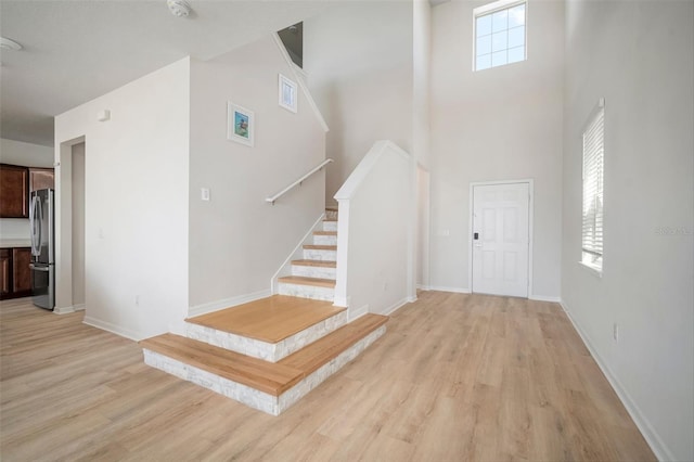 entrance foyer featuring stairs, a high ceiling, light wood-style flooring, and baseboards