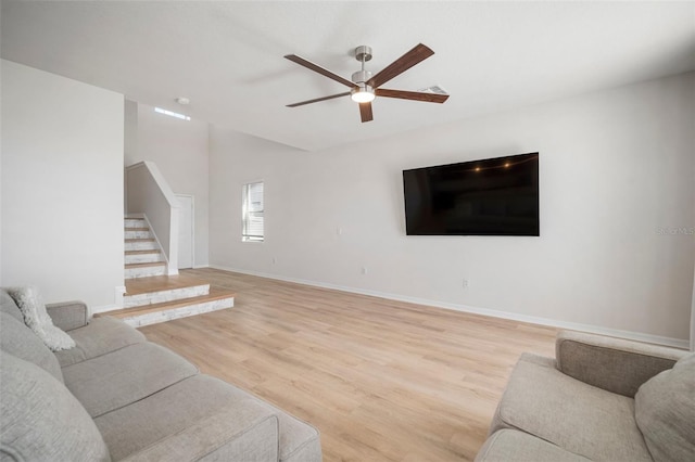 living room featuring baseboards, ceiling fan, light wood-type flooring, stairs, and vaulted ceiling