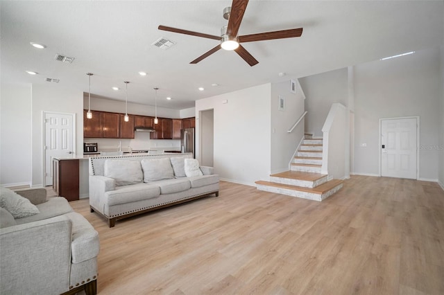 living room with light wood-style floors, stairway, a ceiling fan, and visible vents