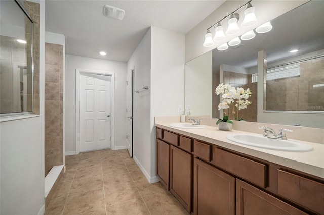 bathroom featuring tile patterned floors, double vanity, a tile shower, and a sink