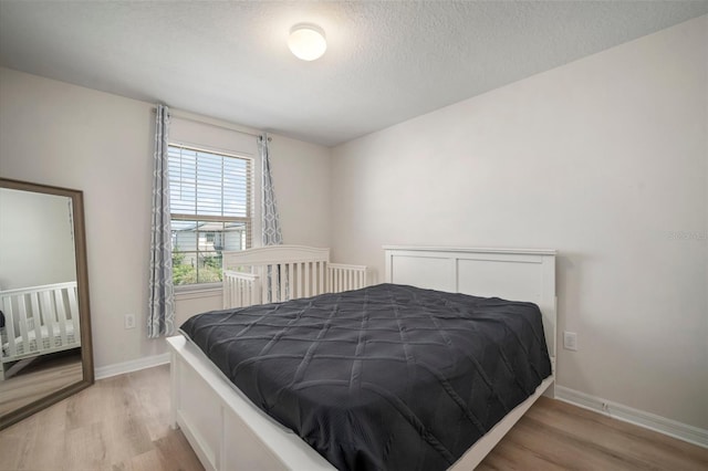 bedroom featuring a textured ceiling, light wood-type flooring, and baseboards