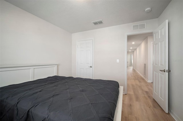 bedroom with light wood-style flooring, baseboards, visible vents, and a textured ceiling