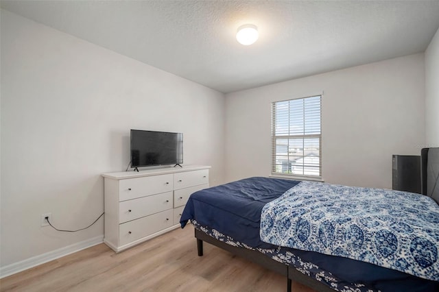 bedroom with light wood-style flooring, baseboards, and a textured ceiling