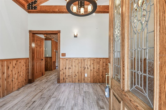 spare room featuring an inviting chandelier, wood finished floors, wood walls, and wainscoting