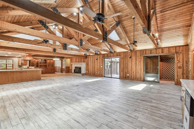 unfurnished living room with beamed ceiling, wood walls, light wood-type flooring, and a ceiling fan