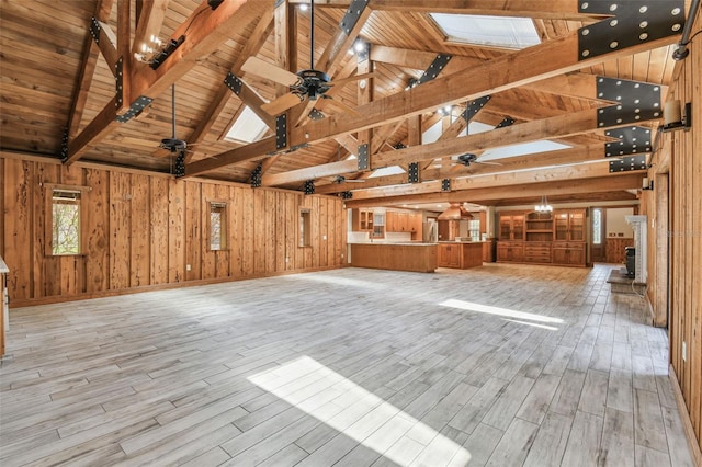unfurnished living room with a skylight, beam ceiling, wooden walls, and ceiling fan