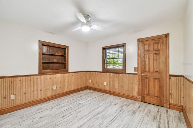 spare room with wooden walls, built in shelves, ceiling fan, wainscoting, and wood finished floors