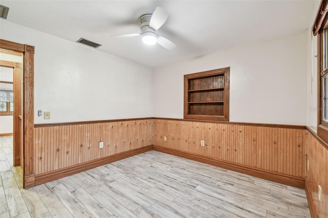 empty room with built in shelves, visible vents, wood finished floors, and a wainscoted wall