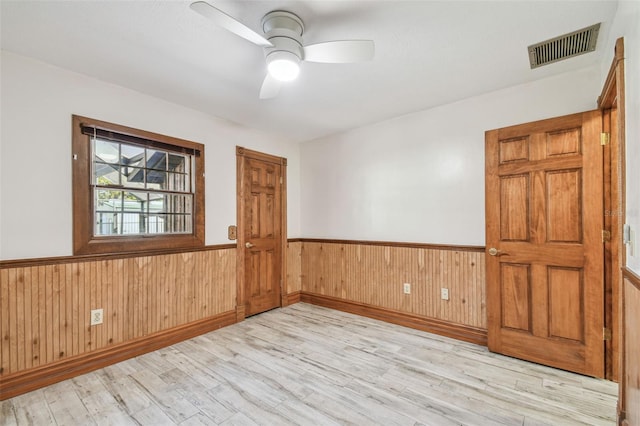 unfurnished room with wooden walls, wood finished floors, a wainscoted wall, visible vents, and a ceiling fan