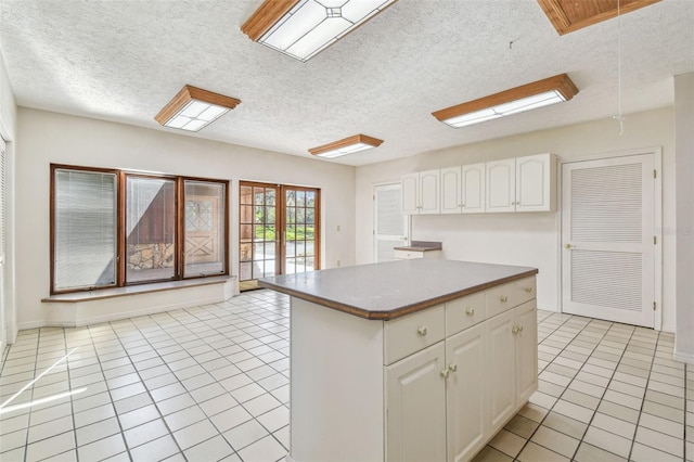 kitchen featuring light tile patterned floors, a kitchen island, a textured ceiling, and white cabinetry