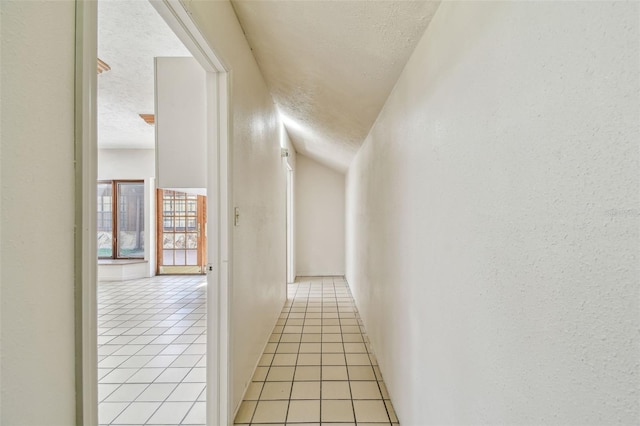 hallway with light tile patterned floors, a textured wall, and a textured ceiling