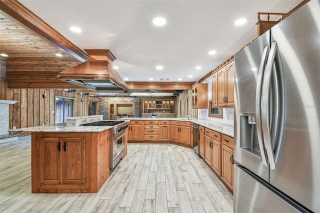 kitchen with stainless steel appliances, light stone countertops, a peninsula, and island range hood