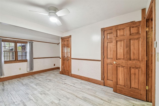 unfurnished room with a textured ceiling, baseboards, light wood-type flooring, and a ceiling fan