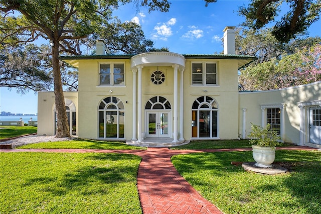 neoclassical home with french doors, a front lawn, a chimney, and stucco siding