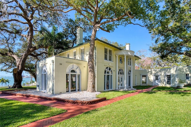 back of property featuring stucco siding, a lawn, and a chimney