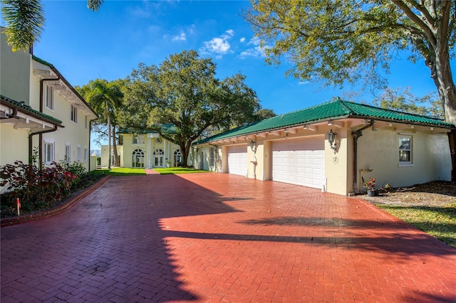 view of front facade with stucco siding, a tiled roof, an attached garage, and decorative driveway