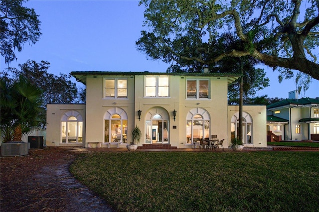 back of house at dusk with stucco siding, a lawn, a patio, french doors, and central AC unit