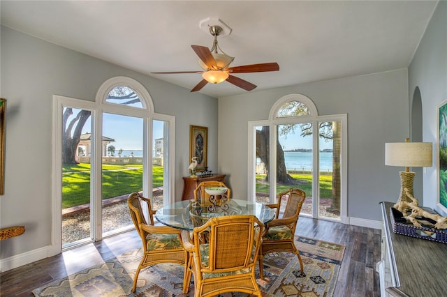 dining space with a ceiling fan, dark wood-style floors, baseboards, and arched walkways