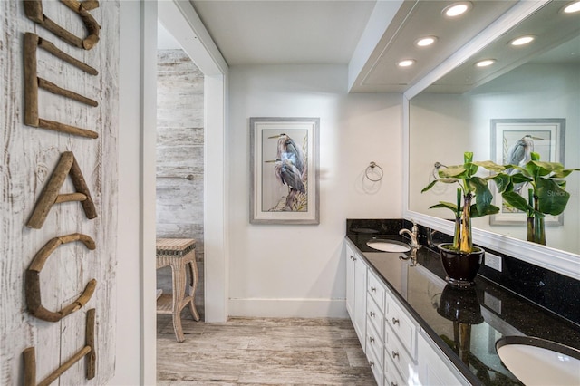 bathroom featuring baseboards, double vanity, recessed lighting, wood finished floors, and a sink